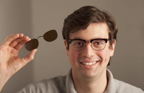 man with sunglass lenses in hand wearing eyeglasses